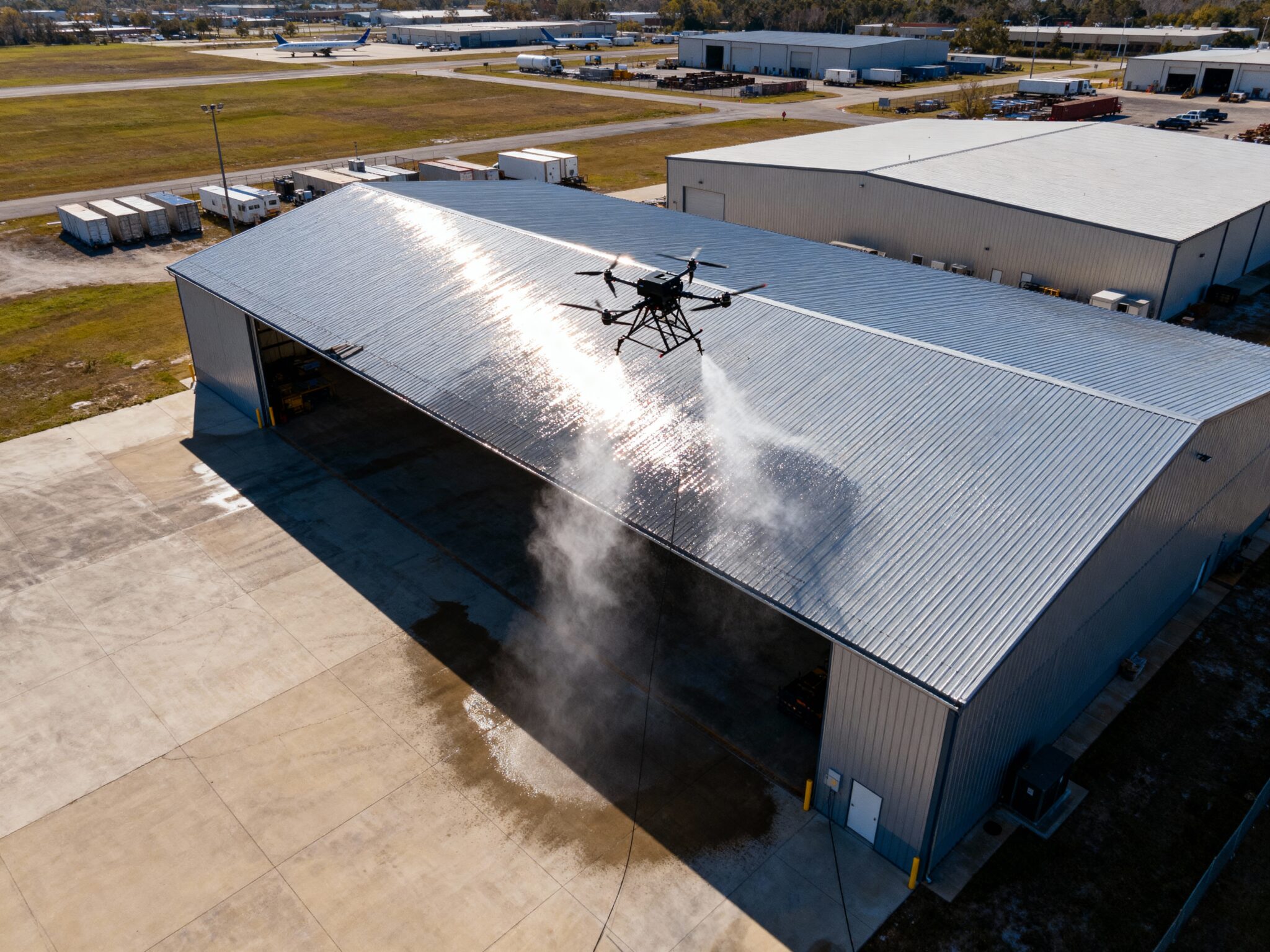 Drone aspergeant eau sur toit hangar métallique.